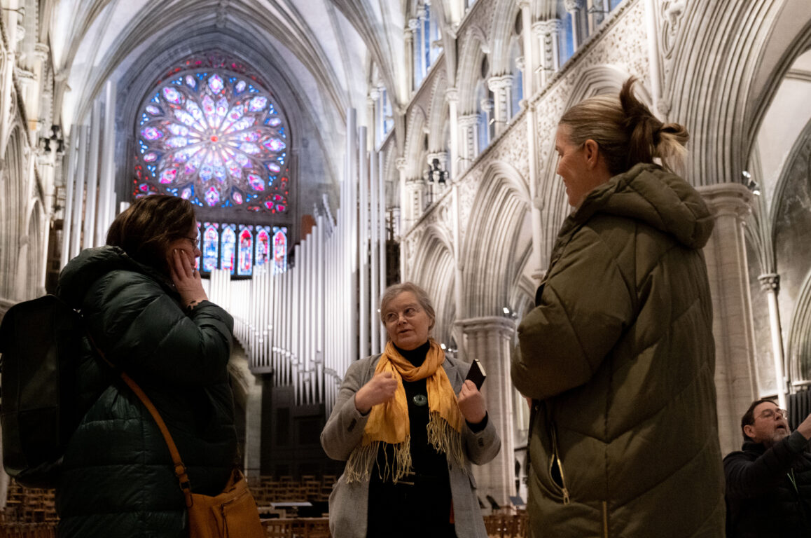 Tre kvinner snakker sammen foran rosevinduet i Nidarosdomen