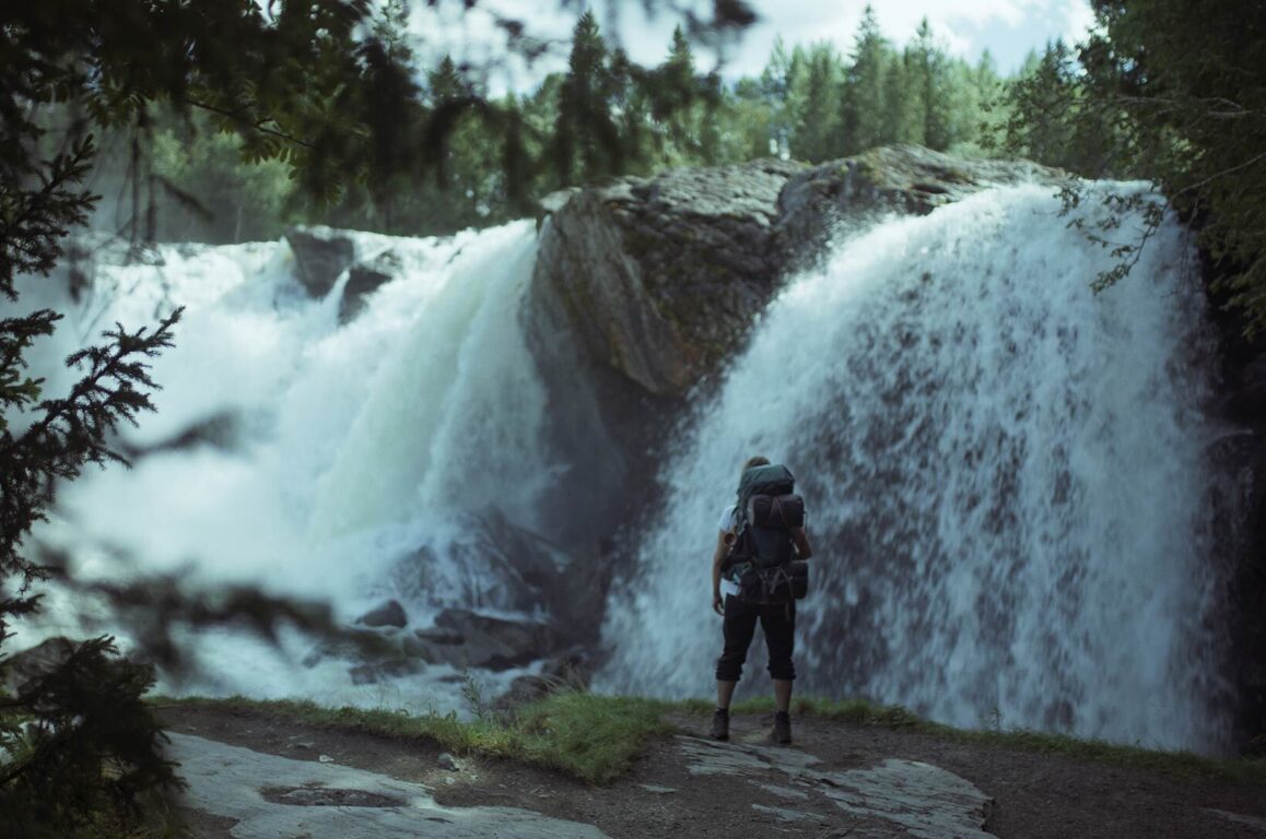 Person med sekk på ryggen foran foss.