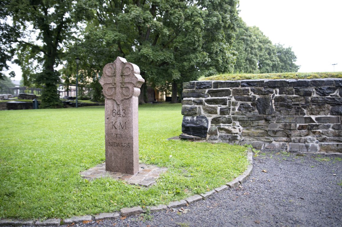 A stone with the pilgrim mark next to an old stone wall. Photo