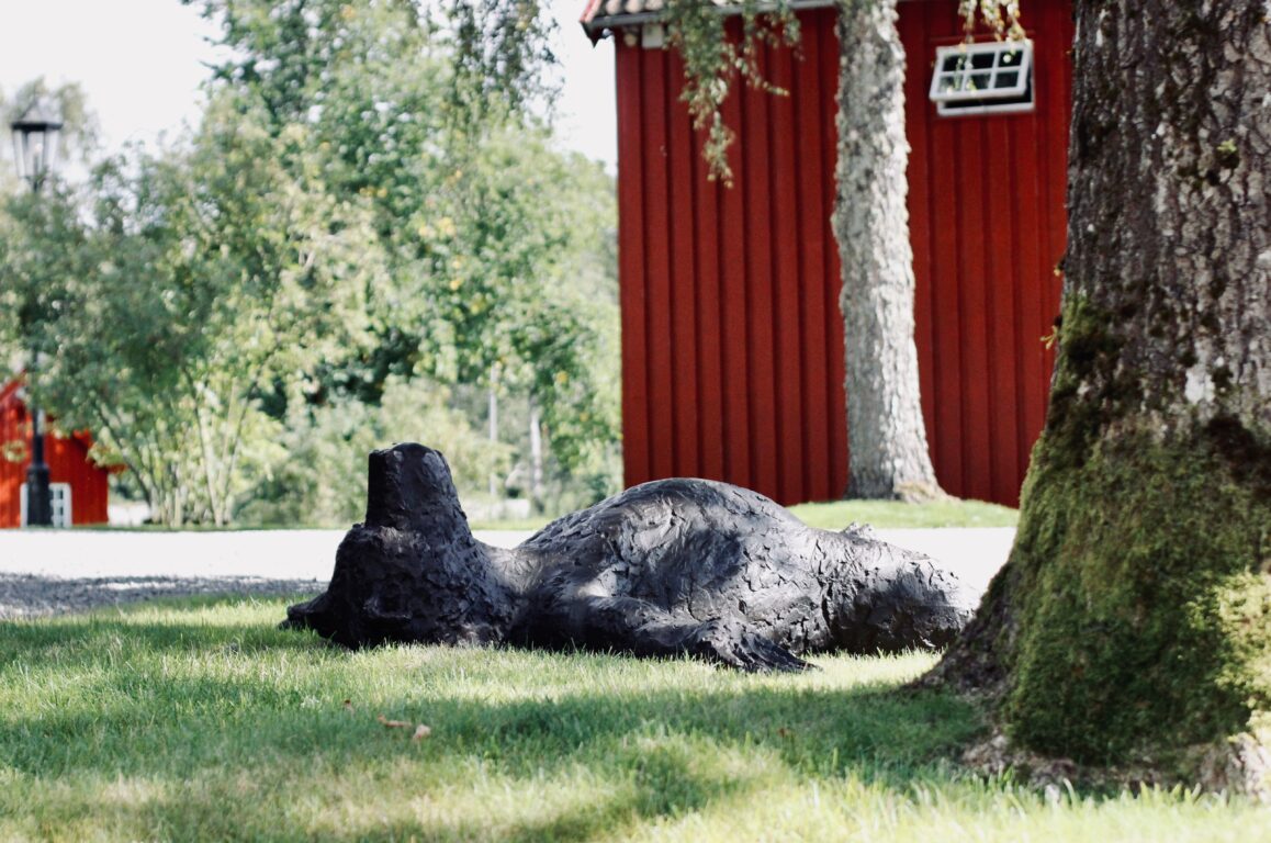 En bjørneskulptur, som ligger rett ut på gresset og nyter solen. FOTO
